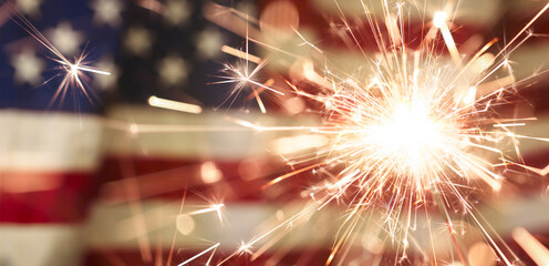 Sparks flying off a burning sparkler in front of the US American flag for patriotic 4th of July...