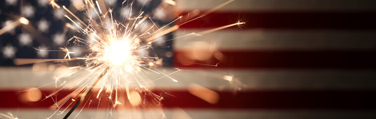 Sparks flying off a burning sparkler in front of the US American flag for patriotic 4th of July celebration.