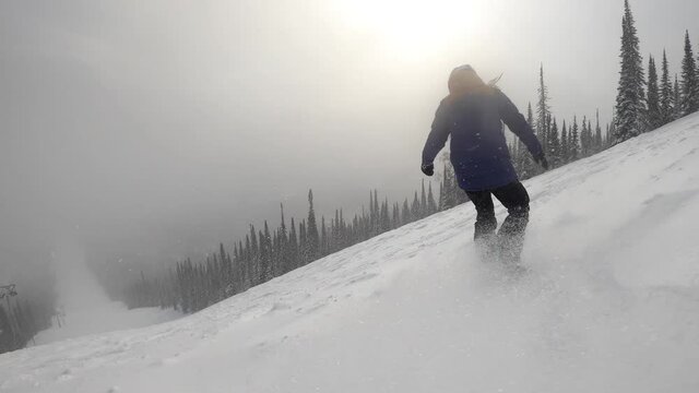 Snowboarder female riding on snow powder from steep slope, winter sunny day in ski resort