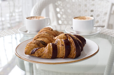 Croissants with chocolate on white plate and cups of coffee close up