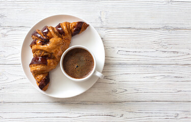 Croissant with chocolate on white plate and cup of coffee