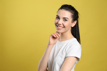 Portrait of happy young woman with beautiful black hair and charming smile on yellow background, space for text - obrazy, fototapety, plakaty