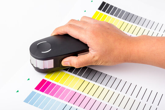 Hand is using the calibration machine on the paper that is printed on the color chart CMYK for test color. calibration machine is essential equipment for the printing industry.