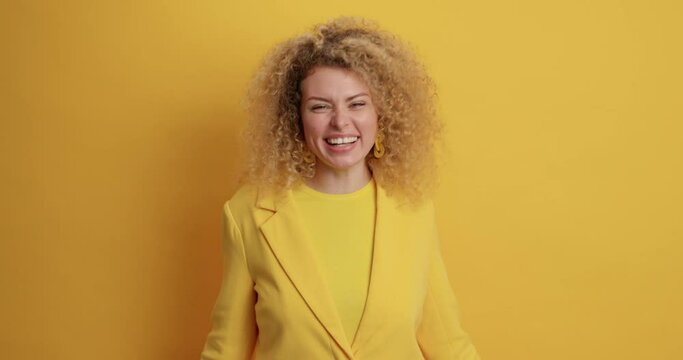 Beautiful romantic curly haired woman blows air kiss keeps palm near mouth smiles positively expresses love to beloved person dressed formally isolated over yellow studio background. Mwah to you