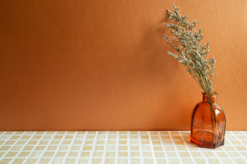 Vase of misty blue dry flowers on beige ceramic mosaic tile table. Orange background. Home interior
