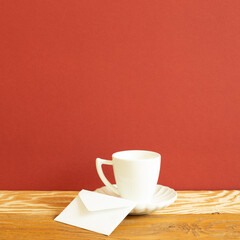 White coffee cup and envelope on wooden table. red background