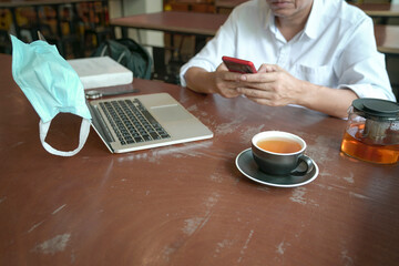 Businessman reading phone with computer and cup of tea on table.  Copy space.
