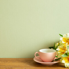 Coffee cup with yellow alstroemeria flowers on wooden table. khaki green background