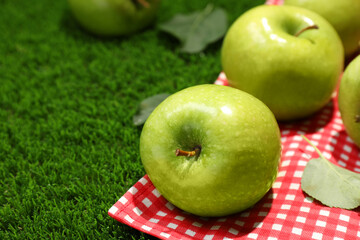 Ripe green apples and picnic blanket on grass, closeup. Space for text