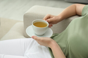 Young woman with cup of hot tea relaxing on sofa, closeup