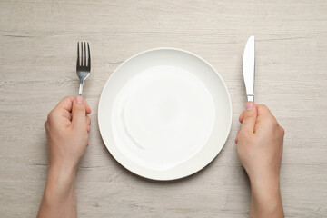 Top view of man with cutlery and empty plate at wooden table, closeup
