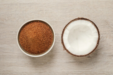Natural coconut sugar in bowl on white wooden table, flat lay