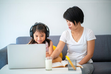 Happy Asian family using laptop computer for online learning a homeschooling in home living room during corona virus pandemic. homeschooling and Asian family concept