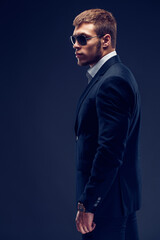 Fototapeta premium Side view of a Fashion bearded young serious man in sunglasses, luxury suit with one hand in pocket