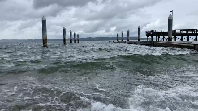 pier on the shore with ocean water waves crashing inder stormy gray clouds
