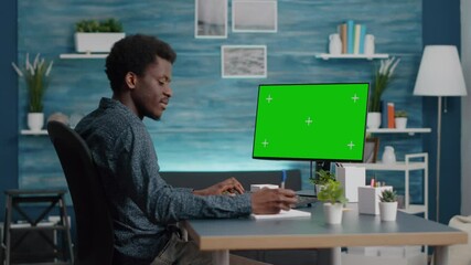 Black man typing and using personal computer with mock up chroma key display, isolated green screen PC for easy replacement. African american guy at home in bright living room - Powered by Adobe