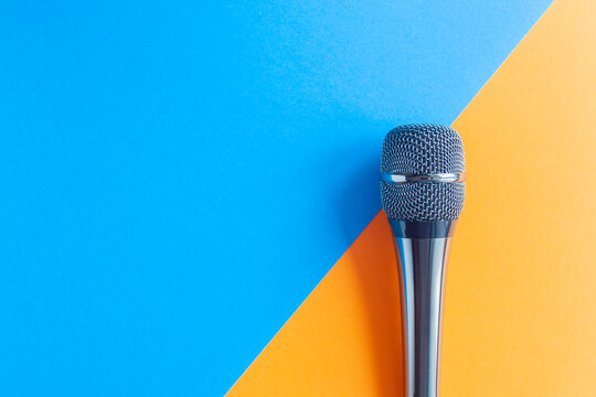 Microphone on a colorful blue and orange geometric background close up. Singing, writing music, karaoke online, creativity, vocals concept, symbol. Singing lessons