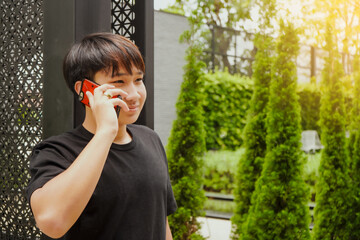 Fototapeta premium Young Asian man smiling, talking on cellphone. Teenager model perform outdoor in beautiful nature environment.