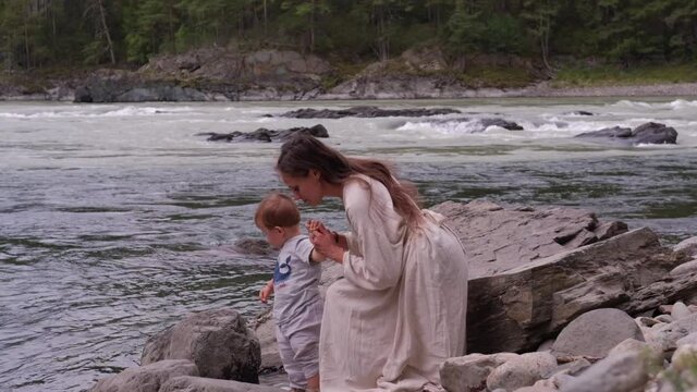 Young mother wearing white dress walking and enjoying  with little kid boy near mountain river outdoor