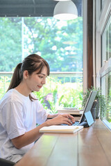 Side view young woman sitting in coffee shop and using computer tablet.