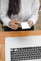 Cropped sot of woman office worker siting in front of laptop computer and using smart phone.