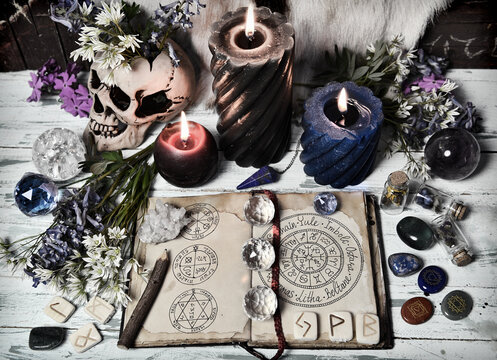 Grunge still life with open witch book, crystal, flowers, burning candles on altar table.
