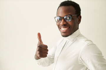 Attractive handsome young black employee with stubble smiling happily, making thumbs up gesture,...