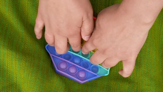 Girl, woman, teenager develops finger motility with colorful poppit game. Close up bunner shot of kid hands playing with colorful pop It fidget toy