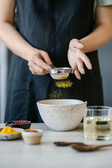 The girl sifts turmeric into a bowl.