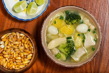 Chicken ginseng soup with broccoli, quail eggs, lemon and toasted peruvian corn. Top view.