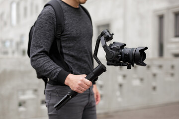 videography, filmmaking and creativity concept - close up of modern dslr camera on 3-axis gimbal stabilizer in male hands over concrete building © Di Studio
