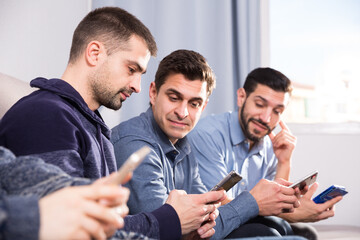 Male friends using mobile gadgets on sofa at home