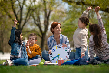 Teacher with small children sitting outdoors in city park, learning group education concept.