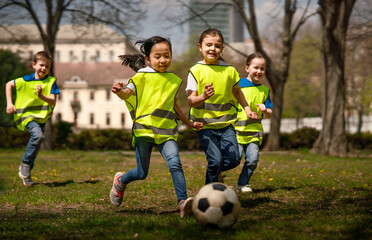 Small children playing football outdoors in city park, learning group education concept.