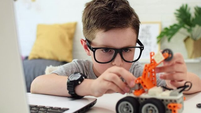 Boy looks with concentration at the robot car and fixes the sensor chip.Child nerd learns coding and programming on a laptop. Robotics, science, mathematics, engineering, technology. STEM education.