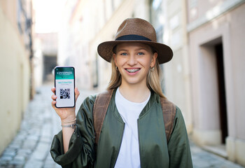 Young woman traveler in city on holiday showing covid-19 vaccine passport on smartphone.