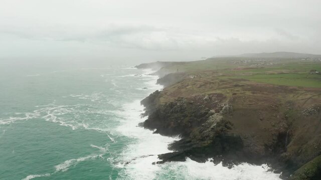 Aerial rotation from the rocky shores of Cornwall toward the misty Atlantic Ocean horizon. 