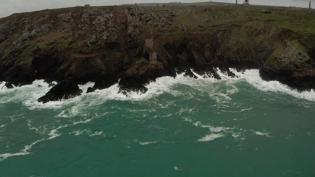 Aerial of strong Atlantic waves crashing on the rocks holding the engine houses of the tin mines of Cornwall. 