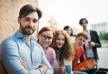 Portrait of young businessman with group of entrepreneurs indoors in office, looking at camera.