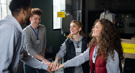 Group of volunteers at work in community charity donation center, stacking hands together.