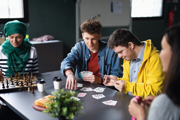 Group of people playing cards and board games in community center, inclusivity of disabled person.