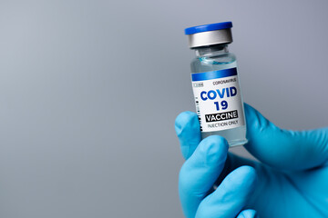 A female doctor wearing blue gloves shows a bottle of covid-19 vaccine on a gray background. Prevent and cure corona virus.