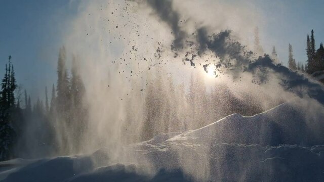 Snow from a snowblower is flying at sunset