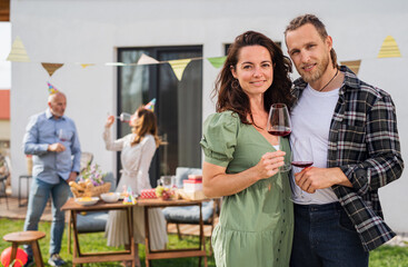Young couple with wine outdoors in garden at home, birthday celebration party.