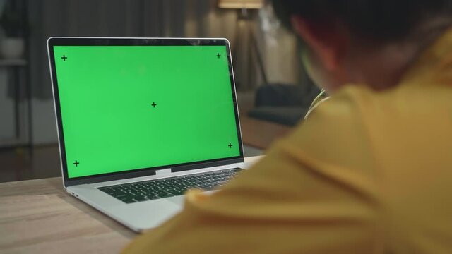Asia Girl Works On A Laptop Computer With Mock-Up Green Screen, In The Background Evening At Home
