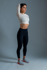 Slim girl doing stretching workout on grey background