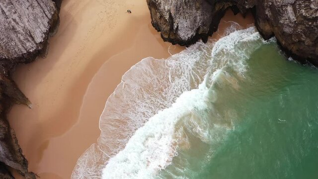 Aerial drone video view on ocean waves with white foam, cliffs, rocks and turquoise water