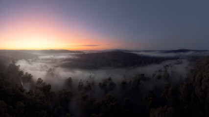 Panoramic aerial view at dawn of Australian countryside with woodlands, fog, hills and sunrise