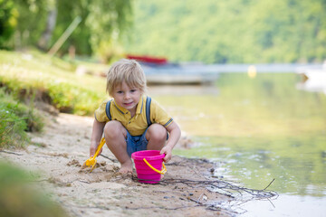 Little toddler child, cute boy, playing with toys in the sand on a lake