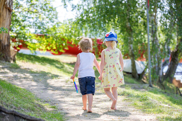 Sweet toddler kids, walking together hand in hand on a little path next to a lake